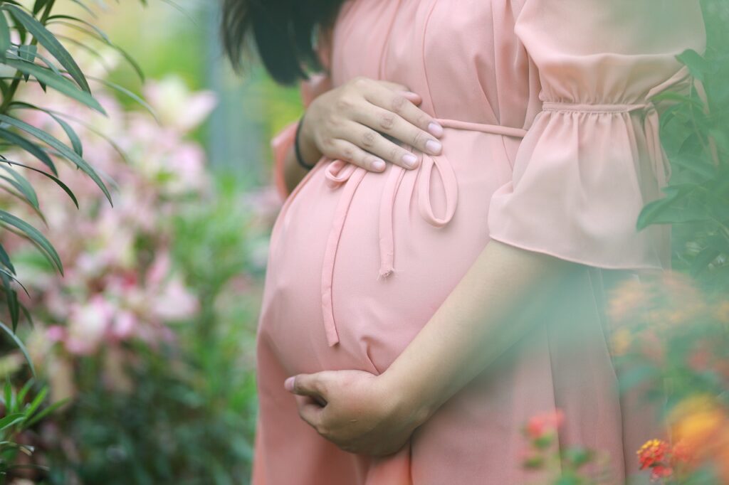 Kobieta w ciąży w różowej sukience w ogrodzie wśród rośliności
