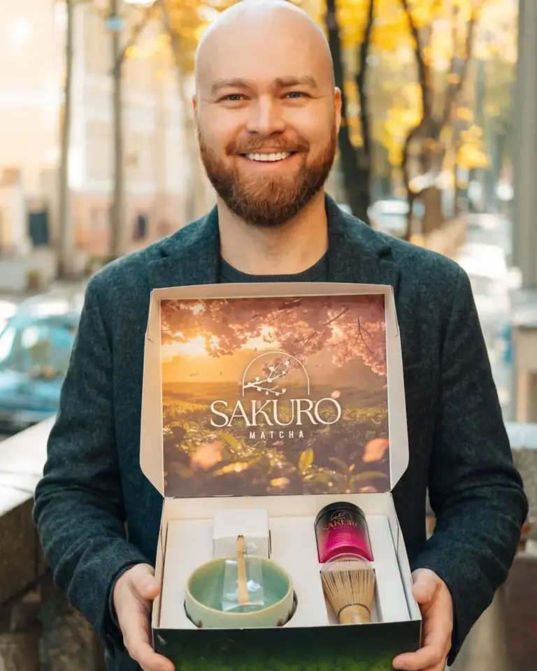 Mężczyzna pokazuje otwarty zestaw Sakuro z czarką, chasenem i puszką matchy