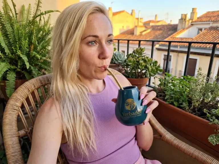Blondynka pije yerba mate z matero Yerbador na balkonie z roślinami o złotej godzinie